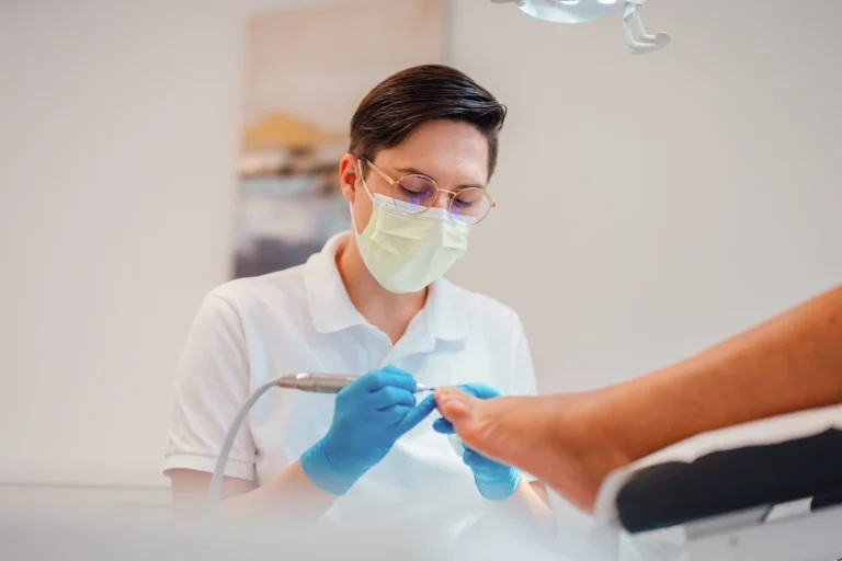 Podologin Madlen mit Maske und Handschuhen bei der fachgerechten Nagelpflege einer Patientin in einem hellen, modernen Behandlungsraum.